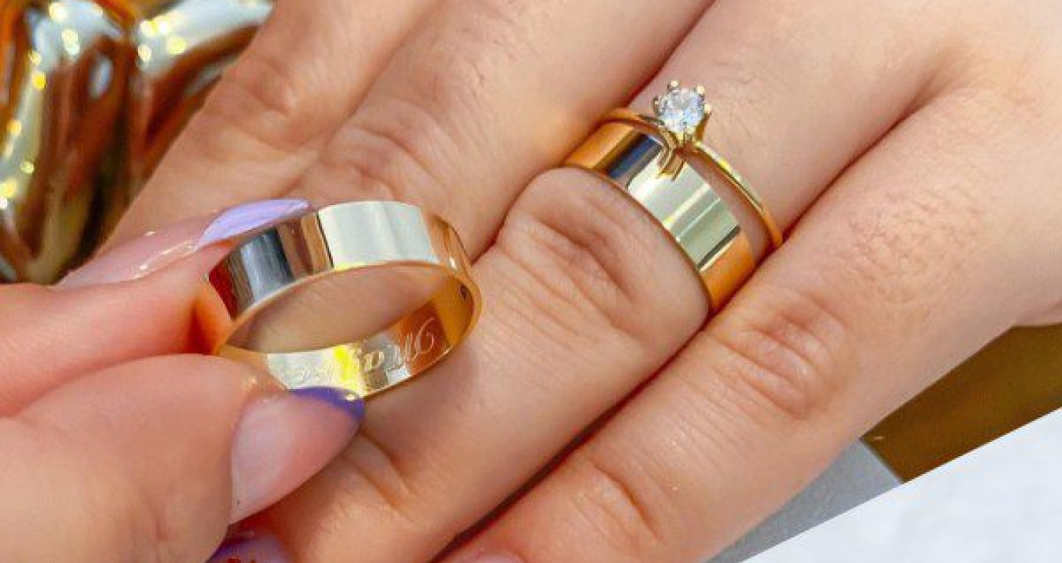 Um anel e duas alianças de ouro 18K sendo usados.